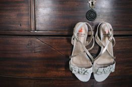 Sandalias blancas con hebillas sobre un mueble de madera oscura.