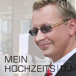 Ein lächelnder DJ mit Brille und Anzug, Hintergrund unscharf. Text: "MEIN HOCHZEITS DJ".