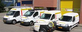 Vier witte bedrijfswagens geparkeerd naast een gebouw met een gele garagedeur.