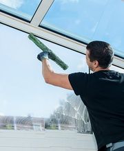 Mann reinigt große Glasfenster mit Blick auf den blauen Himmel.