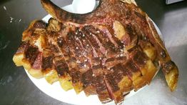 Un gran chuletón asado y cortado en un plato blanco sobre una mesa.