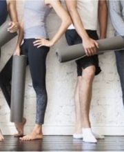Personas con colchonetas de yoga, descalzas, apoyadas en una pared blanca.