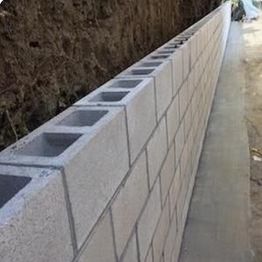 Long cinder block wall under construction along a dirt path.