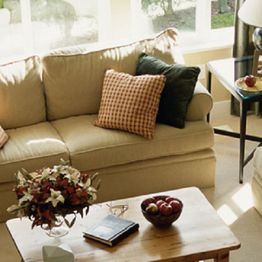 Cozy living room with a beige sofa, patterned pillows, and a wooden table adorned with flowers.