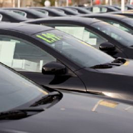 Row of black cars lined up in a dealership parking lot.