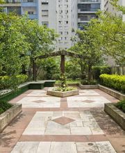 Jardim urbano com bancos, árvores e prédio ao fundo em uma área residencial arborizada.