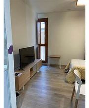 Habitación con televisor, cama, y ventana. Piso de madera clara y paredes blancas.