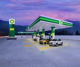 Estación de servicio BP con autos cargando combustible al atardecer, rodeada de montañas.