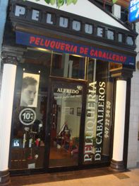 Fachada de una peluquería de caballeros con ofertas y elementos de cuidado personal en la vitrina.