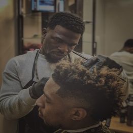Barber styling a client's hair with precision in a well-lit salon, wearing gloves and an apron.