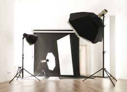 Fotostudio mit Blitzlichtern, Softboxen und schwarzem Hintergrundvorhang auf Holzfußboden.
