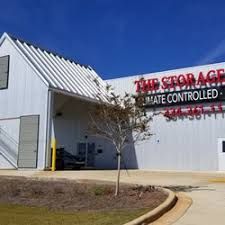 Storage facility with red sign, metal exterior, tree, and blue sky in the background.
