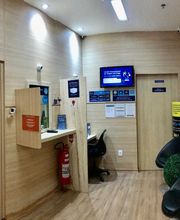 Sala de espera moderna com cadeiras pretas, paredes de madeira e tela de informações na parede.