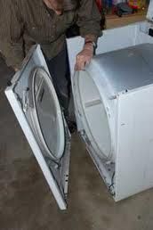 Person repairing an open clothes dryer in a workshop.