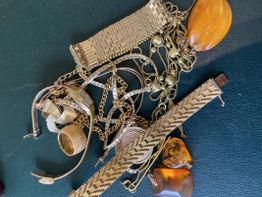 Gold- und Bernsteinschmuck auf einer dunklen Oberfläche verstreut.