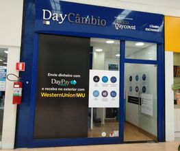 Fachada de uma loja de câmbio chamada DayCâmbio, com anúncios de serviços financeiros.