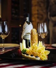 Plato de quesos y frutas con vino y copas en mesa con mantel a rayas.