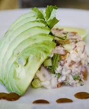 Plato gourmet de aguacate con ensalada de mariscos, adornado con salsas en un plato blanco.