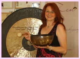 Frau hält eine Klangschale vor einem großen Gong, lächelt, Umgebung mit Zen-Dekoration.