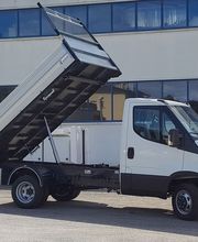 Camion bianco con cassone ribaltabile sollevato in un cortile di fronte a un edificio.
