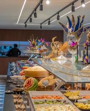 Buffet com pratos variados e decoração colorida, incluindo uma máscara veneziana azul.