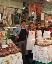 Verkaufsstand mit Wurst- und Käsespezialitäten; vier Verkäufer lächeln in die Kamera.