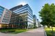 Modern glass office buildings with a tree-lined walkway under a clear blue sky.