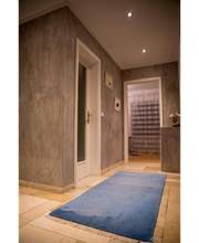 Flur mit grauen Wänden, blauem Teppich, Türen und sanfter Beleuchtung von Einbauleuchten.