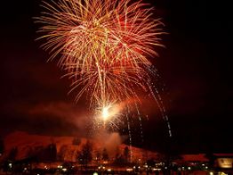 Ein großes Feuerwerk erleuchtet den Nachthimmel über einer Landschaft mit Bäumen und Hügeln.