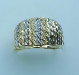 Anel de ouro com textura geométrica e detalhes diagonais em prata, sobre fundo azul claro.