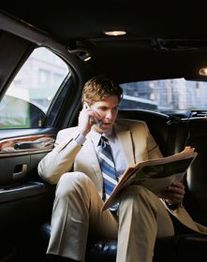 Mann im Anzug telefoniert und liest Zeitung in einem Auto.