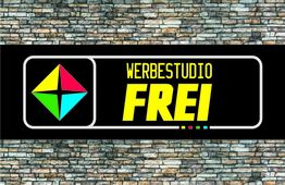 Schild mit "Werbestudio Frei" auf schwarzem Hintergrund, bunter Pfeil, Steinwand als Hintergrund.