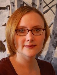 Eine Frau mit kurzen Haaren und Brille vor einem abstrakten, monochromen Hintergrund.