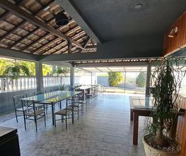 Área externa coberta, com mesas e cadeiras de ferro, vegetação ao fundo e placa de Wi-Fi na parede.