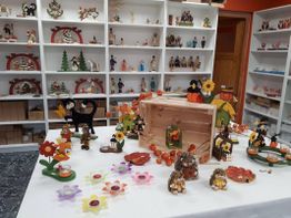 Regale mit Handwerkskunst und Tischdeko: Igel, Blumen, Kürbisse aus Holz in einem Raum.
