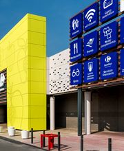 Edificio comercial amarillo con signos azules de servicios y accesos, como WiFi y zona infantil.