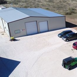 Aerial view of a metal warehouse and parked vehicles on a gravel lot.