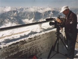 Mann filmt schneebedeckte Berge mit Kamera auf Stativ.