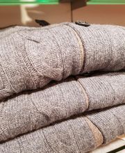 Graue Pullover aus Wolle, dreimal gefaltet und gestapelt auf einem Regal im Geschäft.