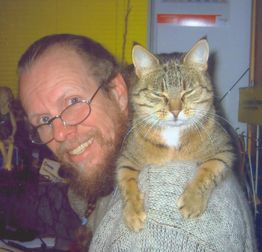 Ein Mann mit Brille lächelt, eine getigerte Katze sitzt auf seiner Schulter und schaut müde.