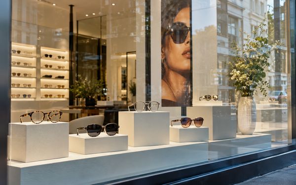 Modernes Schaufenster eines Optikergeschäfts mit stilvoll präsentierten und gezielt ausgeleuchteten Brillengestellen auf hellen Podesten.