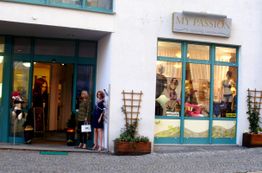 Außenansicht eines Modegeschäfts mit Schaufensterpuppen und Schildern, blau-weiße Fassade.