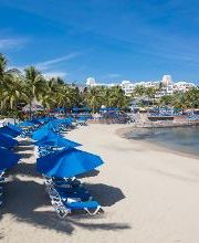Playa tropical con sombrillas azules y palmeras bajo un cielo despejado.