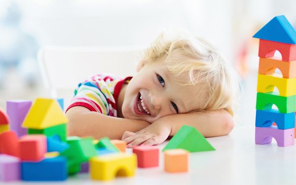 Lachendes Kind sitzt an einem Tisch mit Bauklötzchen