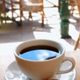 Cup of black coffee on a table in a sunny outdoor cafe setting.