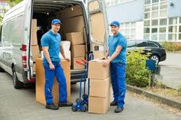Movers in blue uniforms unloading boxes from a van using a dolly.