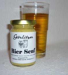 Ein Glas mit Bier und ein Glas mit Görlitzer Bier Senf stehen nebeneinander auf einem Tisch.