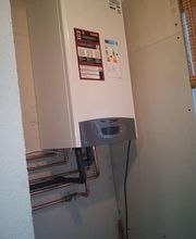 Calentador de agua montado en la pared con conexiones de tuberías visibles a la izquierda.