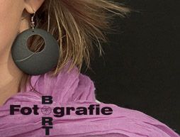 Ein großer, schwarzer Ohrring und lila Schal mit dem Wort "Fotografie" in schwarzer Schrift.