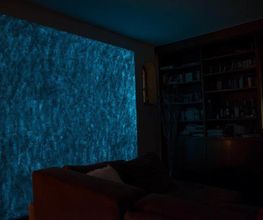 Dunkles Wohnzimmer mit beleuchteter blauer LED-Wand und braunem Sofa im Vordergrund.